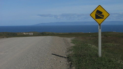 Road sign by sea against sky