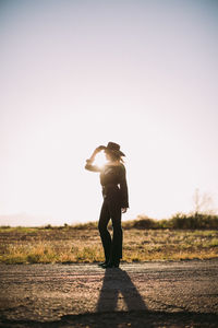 Woman standing in cowboy hat and western wear with sun flare