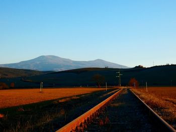 Railroad track leading towards mountains against clear blue sky