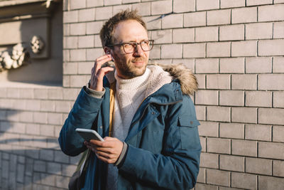 Stylish man with beard and glasses insert wireless headphones into ears. modern technologies concept