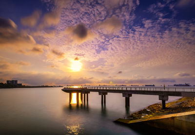 Pier at river against sky during sunset