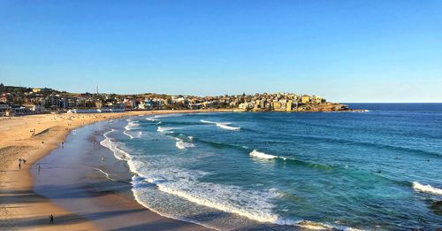 Scenic view of beach by buildings against clear blue sky