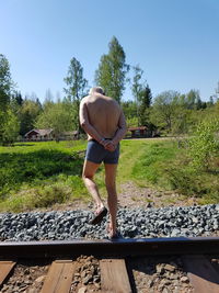 Rear view of shirtless man standing on railroad track