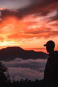 Silhouette man standing on mountain against orange sky