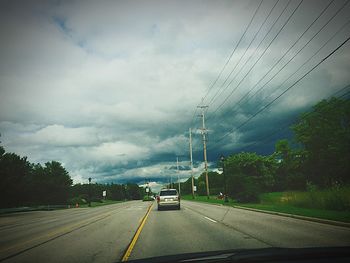 Road passing through highway against cloudy sky