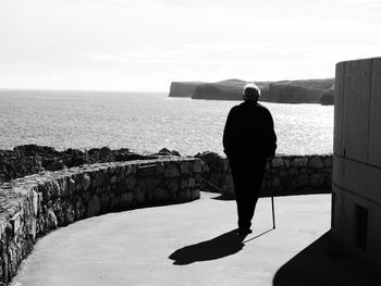 Rear view of silhouette man walking on road by sea during sunny day