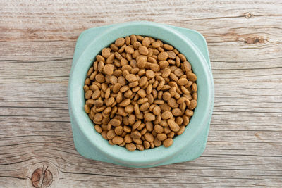 Dry food for cats and dogs in a green bowl on a wooden background. top viev.