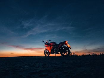 Man riding bicycle on land against sky during sunset