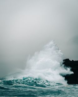 Waves splashing on sea against clear sky