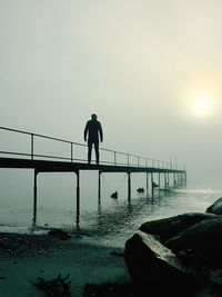 Silhouette man standing on bridge against sky during sunset