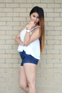 Portrait of a young woman standing against brick wall