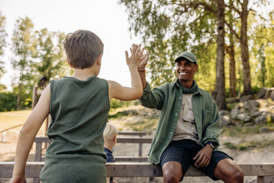 Rear view of boy giving high-five to male camp counselor during summer camp