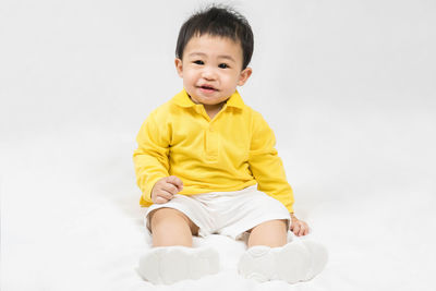 Portrait of cute baby boy sitting against white background