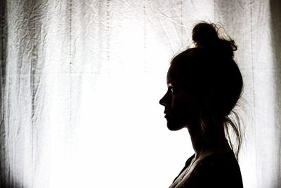 Profile view of thoughtful young woman standing by window curtain