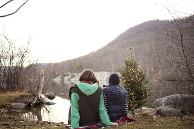 Friends sitting on towel at lakeshore by christmas tree