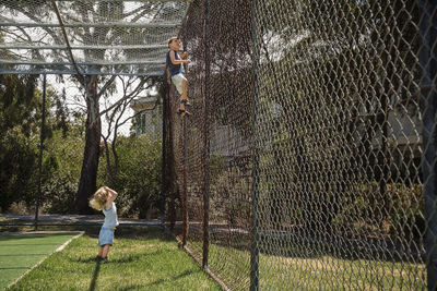 Sister looking at brother climbing fence at park