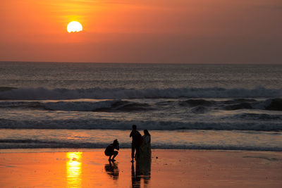 Silhouette people on beach against sky during sunset