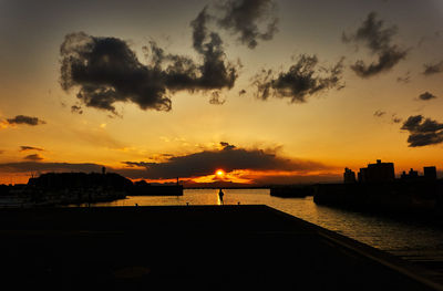 Silhouette city by sea against sky during sunset