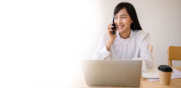 Smiling young woman using laptop on smart phone