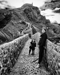 Portrait of smiling mother and daughter standing on bridge at san juan de gaztelugatxe