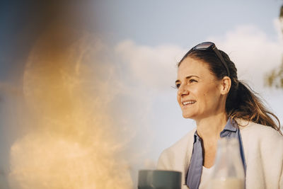 Close-up of thoughtful woman having coffee against sky