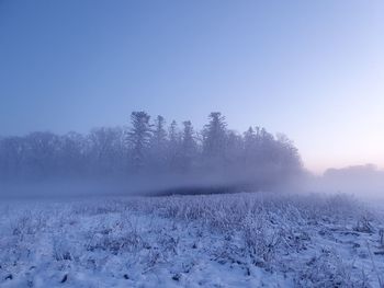 Snow covered landscape with fog against clear sky