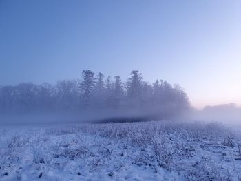 Snow covered landscape with fog against clear sky