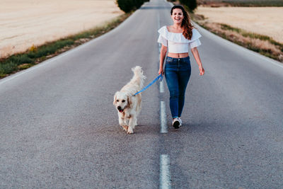 Woman walking with dog on road amidst field