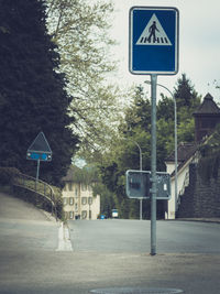 Road sign by trees against sky in city