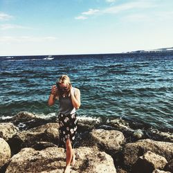 Portrait of young woman standing on rock at sea shore against sky