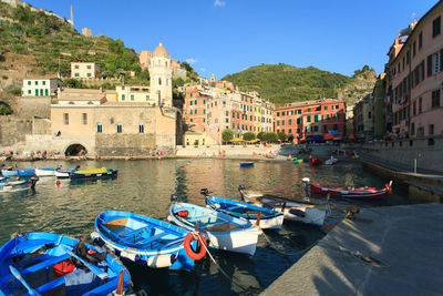 Boats moored in river by city against blue sky