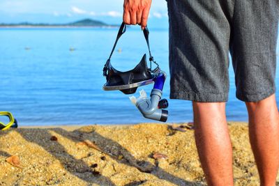 Midsection of man holding scuba mask at beach 