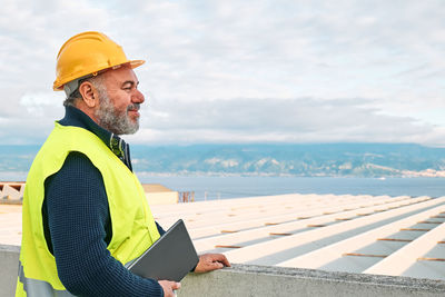 Portrait of smiling middle aged bearded supervisor in hardhat with tablet on building site. 