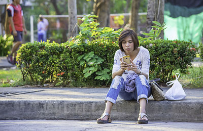 Woman using phone while sitting on seat against plants