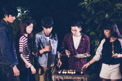 Group of friends roasting food on barbecue at backyard during night