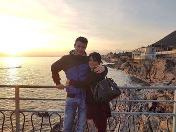 Rear view of man and woman at railing against sky during sunset