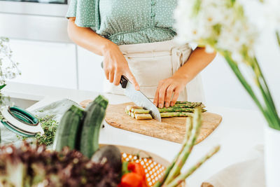 Midsection of a woman cutting asparagus at kitchen counter