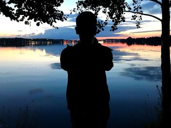 Rear view of silhouette man standing by lake against sky