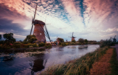 View of traditional windmill by river against sky