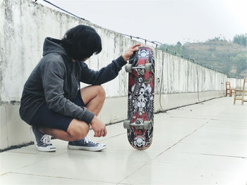 Side view of man sitting on railing against sky