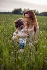 Mom and daughter are sitting in a green field in white t-shirt