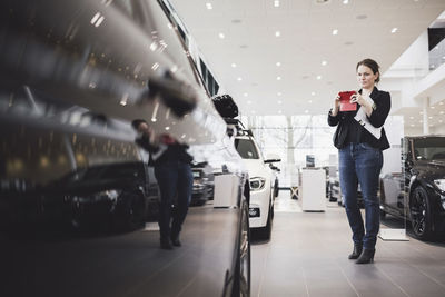 Mature woman photographing new car through mobile phone at showroom