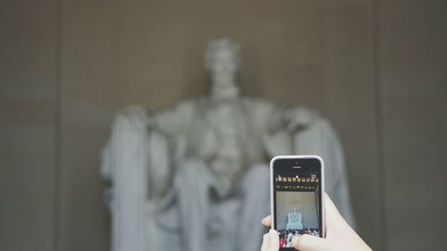 Cropped hand photographing statue of abraham lincoln from smart phone