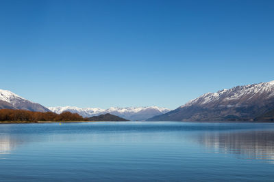 Scenic view of lake and mountains against clear blue sky
