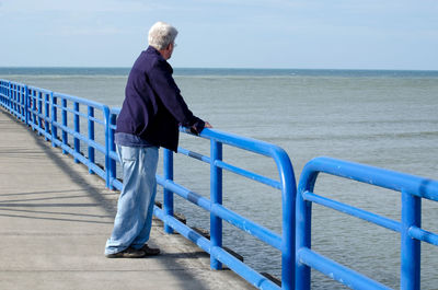 Senior male feeling blue, by blue railing in blue clothing