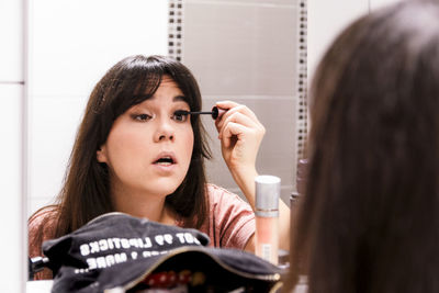 Young woman doing makeup in front of bathroom mirror.