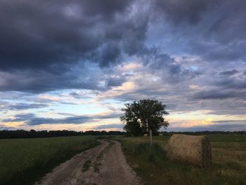 Road amidst field against sky during sunset