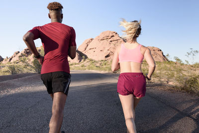 Rear view of hikers running on road against clear sky