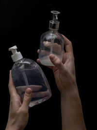 Midsection of person holding glass bottle against black background