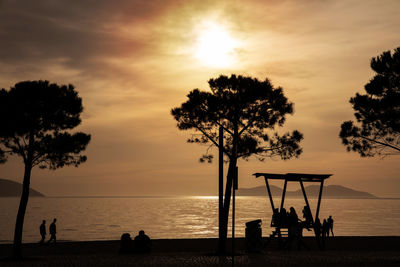 Silhouette people on beach against sky during sunset